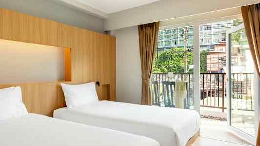 To enkeltsenger i et hotellrom med store glassdører mot en balkong. (AI-generert tekst)