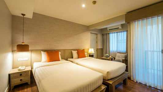 To enkeltsenger med oransje puter i et rom med tre detaljer og gardiner som slipper inn lys. (AI-generert tekst)