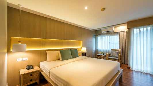 Soverom med en stor seng, sidebord og vindu med gardiner. (AI-generert tekst)