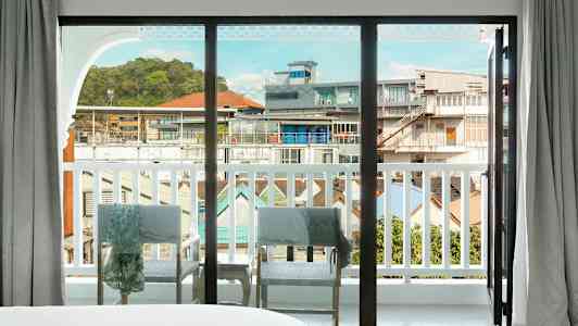 Utsikt gjennom et stort glassvindu som åpner seg mot balkongen med utsikt over bymiljøet. (AI-generert tekst)