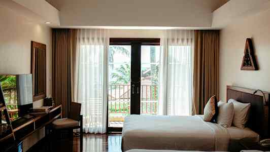 Et hotellrom med to senger, et skrivebord med stol, og store vinduer som vender mot en balkong og trær utenfor. (AI-generert tekst)