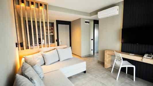 Et moderne hotellrom med sofa, TV og skrivebord, samt en skillevegg for kjøkkenområdet. (AI-generert tekst)