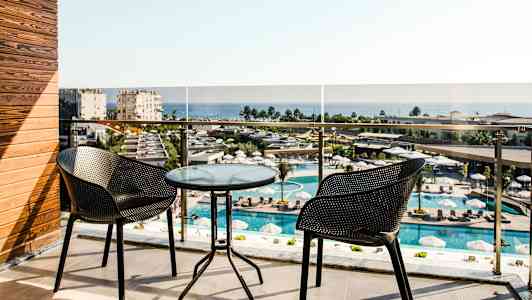 Balkong med to stoler og et glassbord, utsikt over bassengområde og hav. (AI-generert tekst)