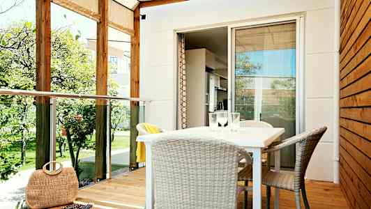 En veranda med tak, bord og stoler samt utsikt mot en hage. (AI-generert tekst)