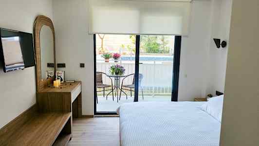 Et hotellrom med en dobbeltseng, skrivebord, TV og en balkong med hagemøbler. (AI-generert tekst)