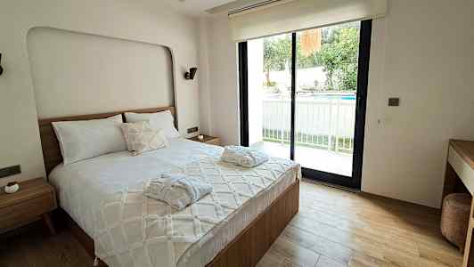 Et soverom med en dobbeltseng, et vindu som vender ut mot en uteplass og et basseng. (AI-generert tekst)