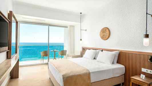 Hotellrom med en dobbeltseng og balkong med utsikt over havet. (AI-generert tekst)