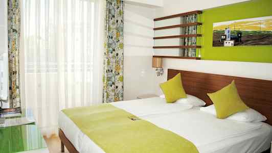 Et hotellrom med en dobbeltseng og grønt sengetøy. (AI-generert tekst)