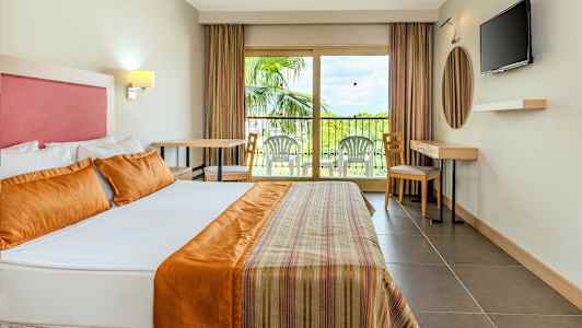 Interiør av et hotellrom med en stor seng, en balkong med utemøbler og en TV på veggen. (AI-generert tekst)