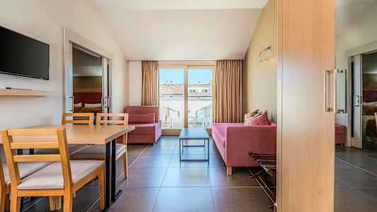 Stue med røde sofaer, et spisebord og stoler, en TV på veggen og balkongdører som fører til en terrasse. (AI-generert tekst)