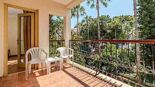 Balkong med en dør, to hvite plaststoler og utsikt over trær og vegetasjon. (AI-generert tekst)