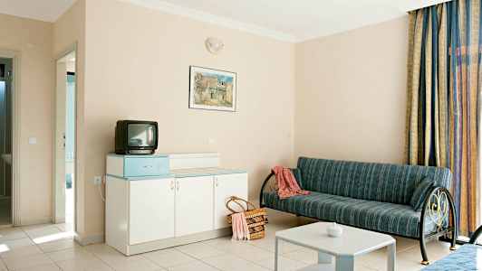 Hotellrom med sofa, bord, skap og liten TV. (AI-generert tekst)