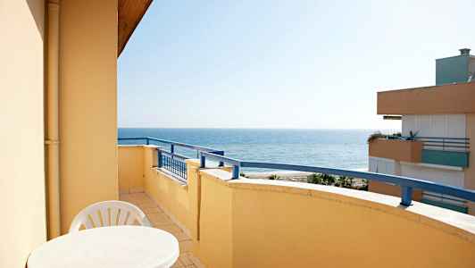 En balkong med bord og stoler, med havutsikt. (AI-generert tekst)