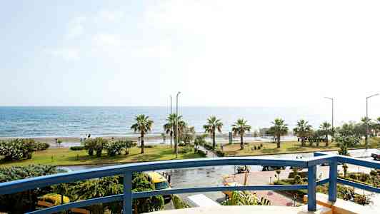 Utsikt fra en balkong mot en kystlinje med palmer og hav. (AI-generert tekst)
