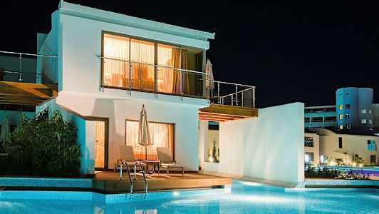 Hvit bygning med basseng foran, tatt om kvelden. (AI-generert tekst)