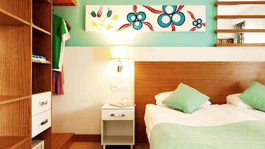 Et soverom med en seng, to grønne puter, et tremøbel skap og et nattbord med en lampe. (AI-generert tekst)