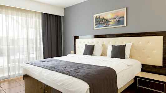 Et moderne hotellrom med en dobbeltseng, en grå sengepute og et maleri på veggen. (AI-generert tekst)