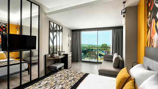 Moderne hotellrom med seng, sofa og utsikt mot balkong med panoramautsikt. (AI-generert tekst)