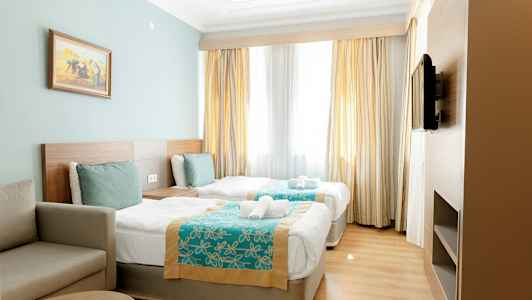 Hotellrom med to enkeltsenger, en sofa og en TV på veggen. (AI-generert tekst)