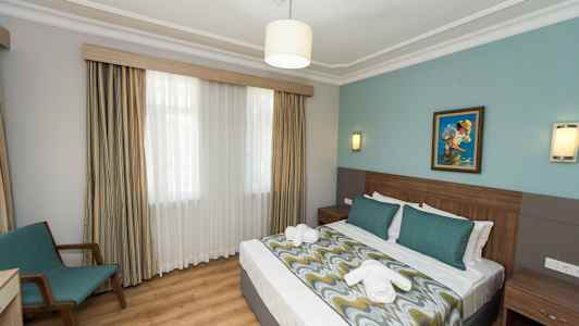 Hotellrom med dobbeltseng, sengelamper, et maleri på veggen og en stol ved vinduet. (AI-generert tekst)