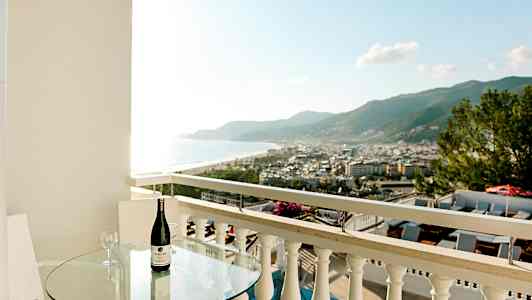 Balkong med glassbord, flaske vin og utsikt over by og kyst. (AI-generert tekst)