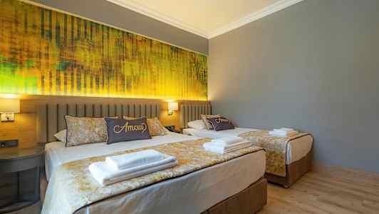 To senger i et hotellrom med grå vegger og gul innredning. (AI-generert tekst)