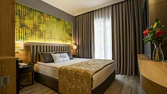 Et hotellrom med en dobbeltseng, grå gardiner og et maleri over sengen. (AI-generert tekst)