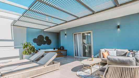 En terrasse med solsenger, sofa og bord under et pergolatak. (AI-generert tekst)