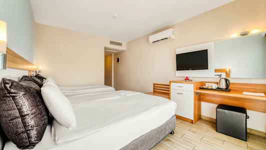 Et hotellrom med to senger, et skrivebord, et speil og en veggmontert TV. (AI-generert tekst)