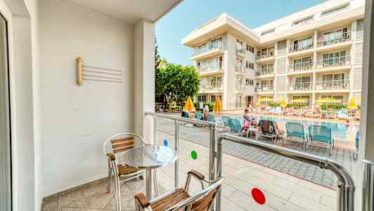 En balkong med bord og stoler vender mot et basseng og et hotell. (AI-generert tekst)