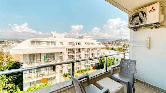 Utsikt fra en balkong med stoler og bord, med utsikt over en boligblokk. (AI-generert tekst)