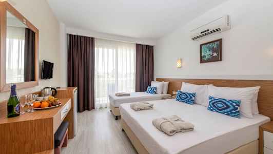 Hotellrom med to enkeltsenger oppredd med hvite laken og blå puter, samt et bord med frukt og drikkevarer. (AI-generert tekst)