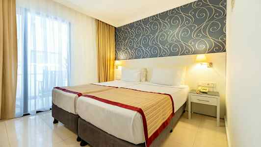 Hotellrom med to enkeltsenger, dekorativt tapetmønster og vindu med gardiner. (AI-generert tekst)