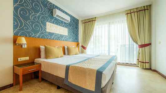 Hotellrom med dobbeltseng, blå og gullfarget innredning samt vindu med lyse gardiner. (AI-generert tekst)