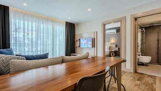 Interiør av et moderne hotellrom med bord, sofa, TV og tilstøtende soverom og bad. (AI-generert tekst)