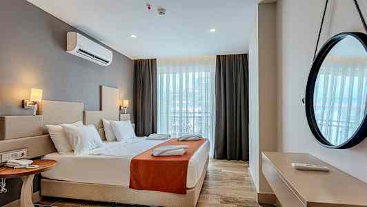 Et hotellrom med en dobbeltseng, nattbord, dekorativt speil på veggen og vindu med gardiner. (AI-generert tekst)