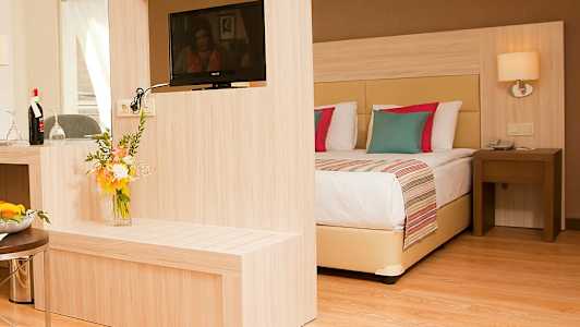 Et hotellrom med moderne innredning, inkludert en dobbeltseng, en TV på en trebjelke og en blomsterbukett. (AI-generert tekst)