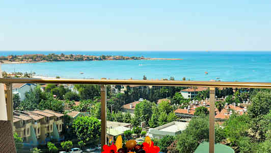 Utsikt fra en balkong over havet og bebyggelse med trær og bygninger. (AI-generert tekst)