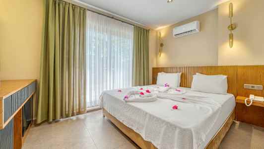 Hotellrom med en dobbeltseng redd opp med hvite laken og dekorert med blomster. (AI-generert tekst)