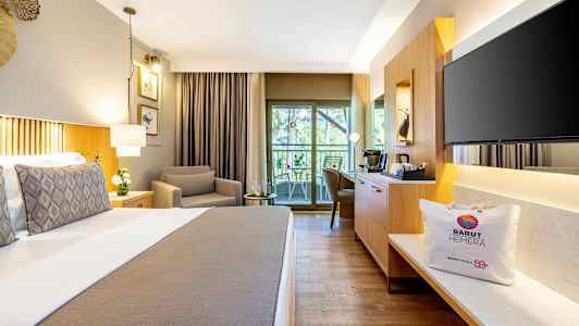 Et hotellrom med en komfortabel seng, en lenestol, en sittegruppe ved balkongen og moderne møbler. (AI-generert tekst)