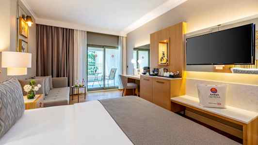 Et velmøblert hotellrom med en dobbeltseng, sittegruppe, skrivebord og en balkong. (AI-generert tekst)