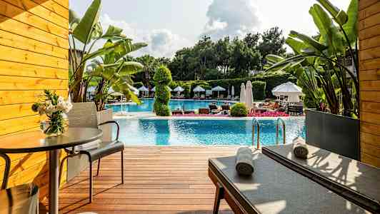 Terrasse foran et basseng med solsenger, bord og planter. (AI-generert tekst)