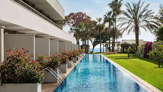 Langt basseng med omkringliggende grøntområder og moderne bygninger. (AI-generert tekst)