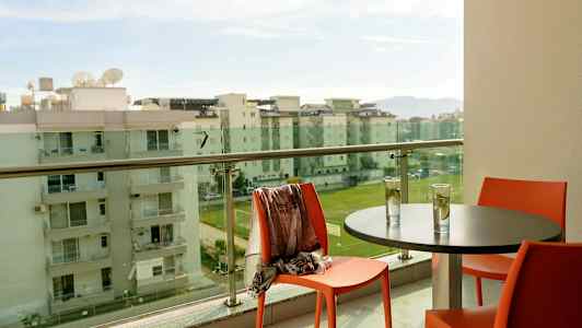 En balkong med sitteplasser, et bord med to glass og en utsikt over hotellbygninger. (AI-generert tekst)