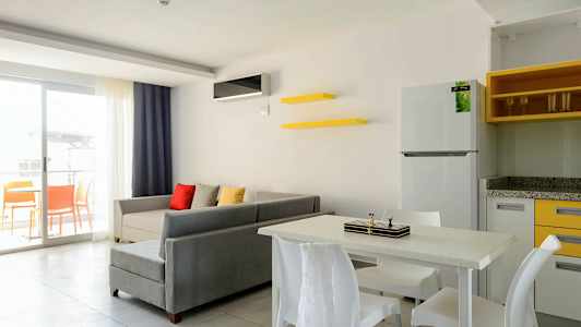 En stue med grå sofa, fargerike puter, spisebord med stoler og en åpen balkong. (AI-generert tekst)