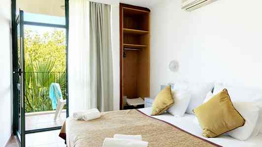 Et hotellrom med en oppredd seng, åpen skap og en balkongdør som fører ut til en uteplass. (AI-generert tekst)