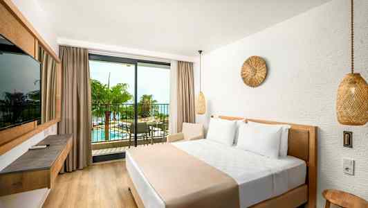 Et hotellrom med en stor seng og en balkong med utsikt over et basseng og palmetrær. (AI-generert tekst)