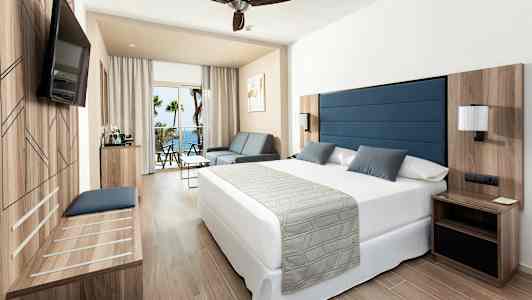 Rom med dobbeltseng, sittemøbler og balkong med havutsikt. (AI-generert tekst)