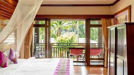 Hotellrom med seng, myggnett, balkong og utsikt over grønne omgivelser. (AI-generert tekst)