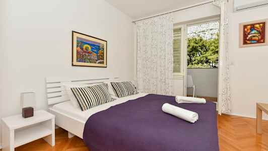 Et soverom med en dobbeltseng, lilla sengeteppe og to foldede håndklær. (AI-generert tekst)